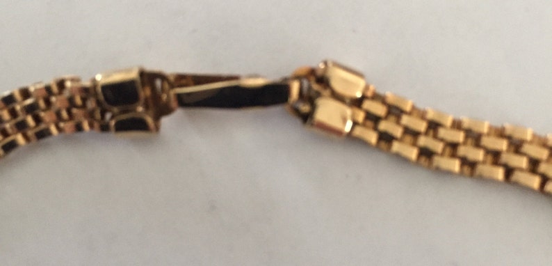 May include: A gold chain bracelet with a box clasp. The chain is made of small, square links.