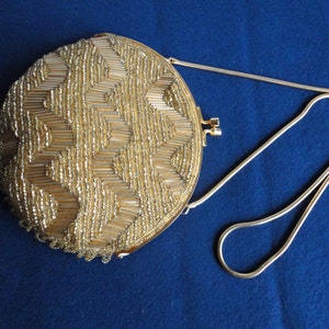 May include: A gold round beaded evening bag with a gold chain strap. The bag is decorated with a geometric pattern of beads.