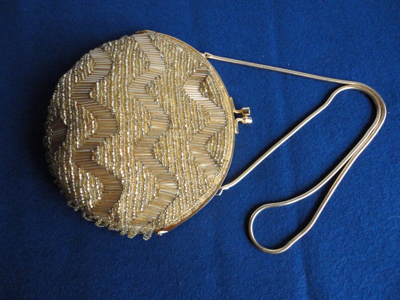 May include: A gold round beaded evening bag with a gold chain strap. The bag is decorated with a geometric pattern of beads.