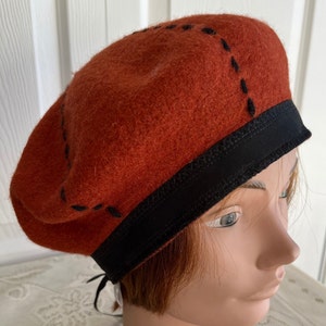May include: A rust-colored beret with a black ribbon and black stitching around the edge. The beret is on a mannequin's head.