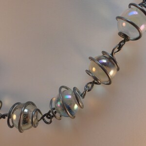 May include: A silver wire necklace with iridescent glass beads. The beads are encased in wire spirals.