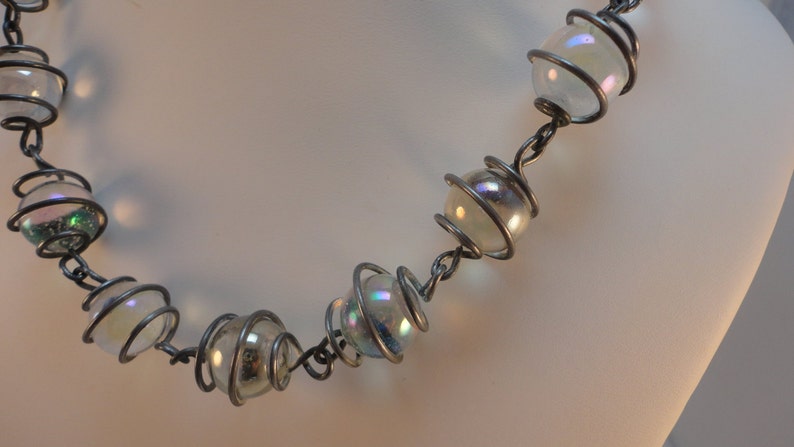 May include: A silver wire necklace with iridescent glass beads. The beads are encased in wire spirals.