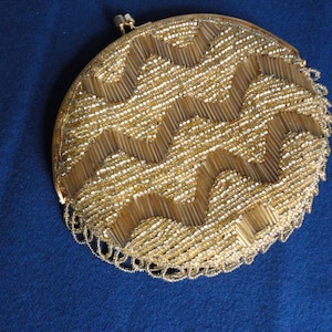 May include: A round, gold-colored beaded clutch purse with a fringe detail. The beads are arranged in a geometric pattern.
