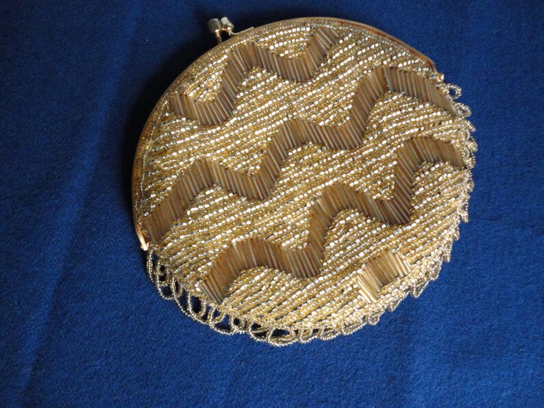 May include: A round, gold-colored beaded clutch purse with a fringe detail. The beads are arranged in a geometric pattern.