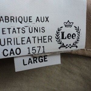May include: A white tag with black text that reads "Fabrique aux Etats Unis Curileather CAO 1571 Large" and a Lee logo with a crown and wreath.