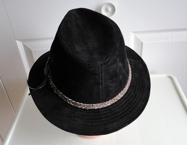 May include: A black suede fedora hat with a brown and white patterned band around the crown.