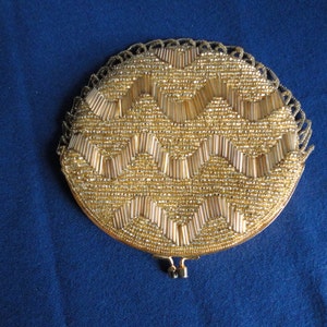 May include: A round, gold-colored beaded purse with a zig-zag pattern. The purse has a metal clasp and a beaded fringe.