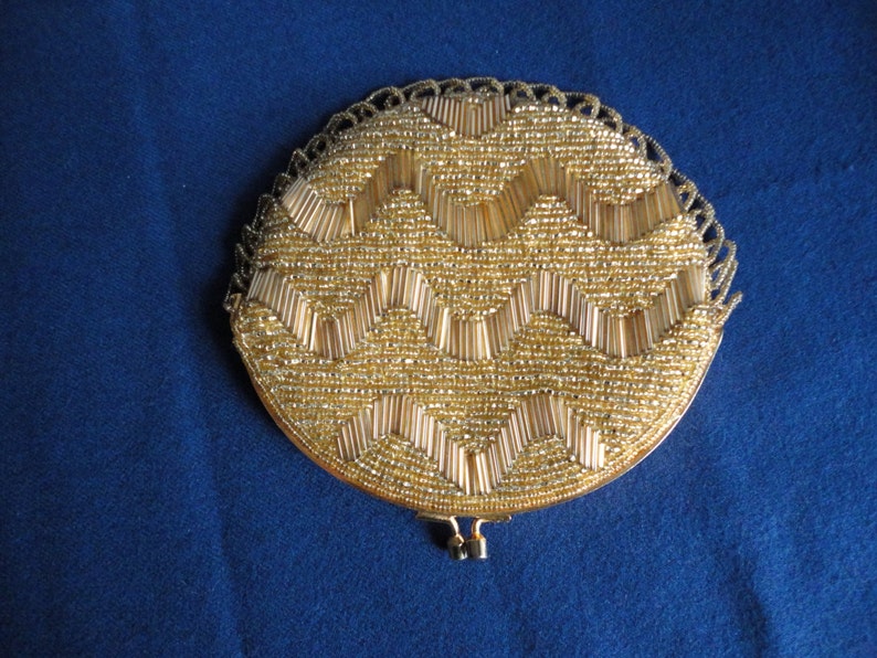 May include: A round, gold-colored beaded purse with a zig-zag pattern. The purse has a metal clasp and a beaded fringe.