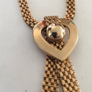 May include: A gold chain necklace with a heart-shaped pendant. The pendant has a round, gold-toned center piece.