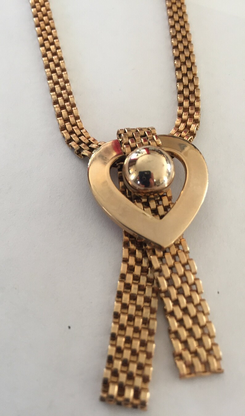 May include: A gold chain necklace with a heart-shaped pendant. The pendant has a round, gold-toned center piece.