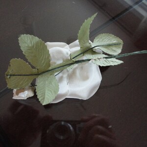Puede incluir: Una rosa de papel blanco con hojas de papel verde unidas a un tallo marr&oacute;n.