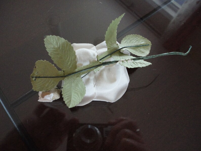 Puede incluir: Una rosa de papel blanco con hojas de papel verde unidas a un tallo marr&oacute;n.