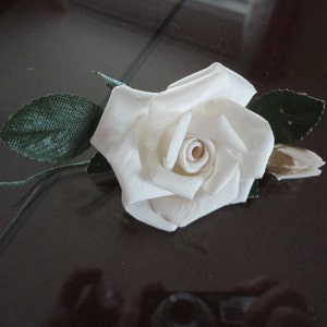 Puede incluir: Una sola rosa blanca de tela con hojas verdes. La rosa es un dise&ntilde;o simple y elegante.