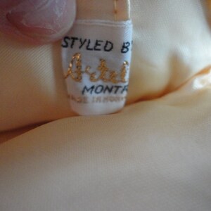 May include: A white satin clutch bag with a gold chain strap. The bag has a label that reads "Styled by Artel, Mont-R, Made in Hong Kong".