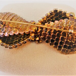 May include: A gold-toned brooch with a bow design made of iridescent glass stones. The brooch has a pin and catch closure.