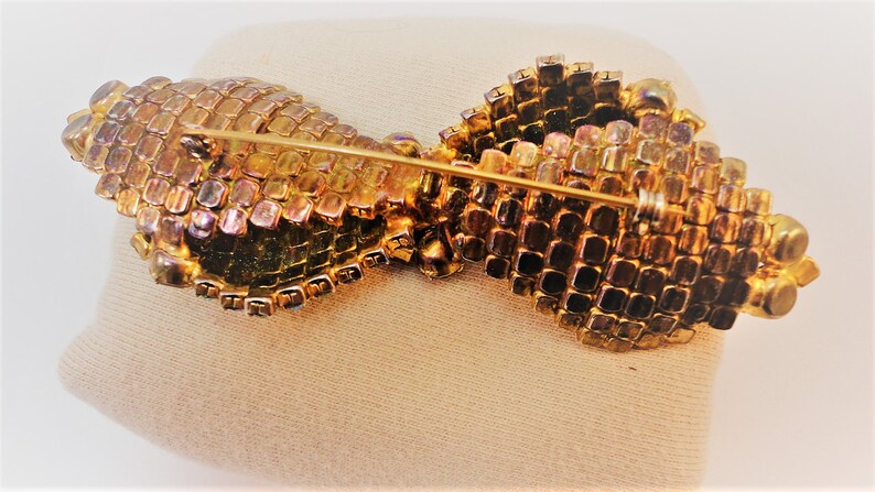 May include: A gold-toned brooch with a bow design made of iridescent glass stones. The brooch has a pin and catch closure.