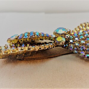 May include: A gold tone brooch with iridescent rhinestones in a floral design. The brooch has a pin back.