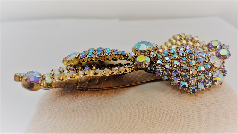 May include: A gold tone brooch with iridescent rhinestones in a floral design. The brooch has a pin back.
