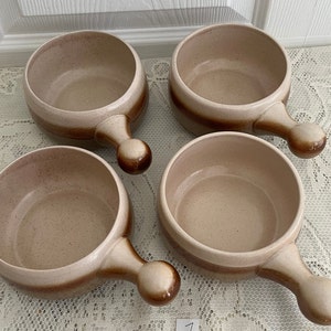 Peut inclure: Quatre bols en céramique brun et beige avec des anses. Les bols ont un glaçage moucheté et sont parfaits pour servir des soupes ou d'autres plats.
