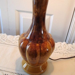 May include: A brown and yellow ceramic table lamp with a bulbous base and a brown and yellow glaze. The lamp has a simple design and a classic look.