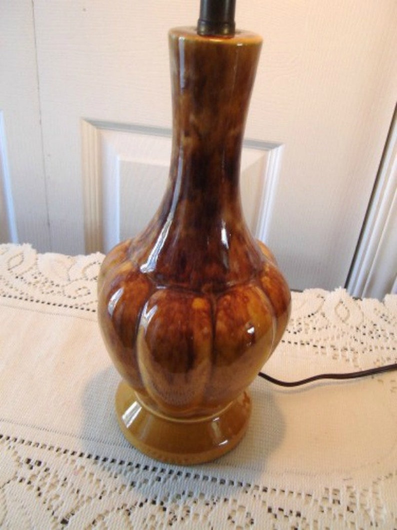 May include: A brown and yellow ceramic table lamp with a bulbous base and a brown and yellow glaze. The lamp has a simple design and a classic look.