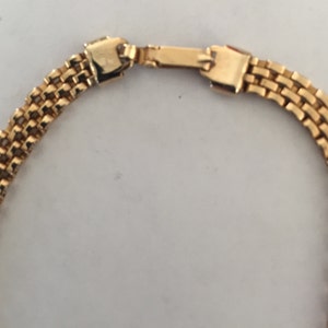 May include: A gold chain necklace with a box clasp closure. The chain is made of multiple rows of small, linked squares.
