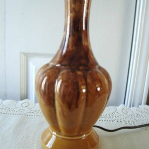 May include: A brown and tan ceramic table lamp with a bulbous base and a slender neck. The lamp has a mottled glaze and a ribbed texture.