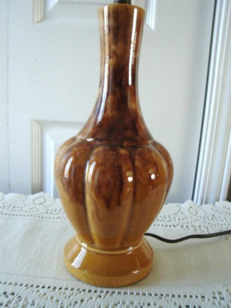 May include: A brown and tan ceramic table lamp with a bulbous base and a slender neck. The lamp has a mottled glaze and a ribbed texture.