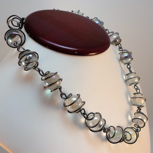 May include: A silver necklace with iridescent glass beads encased in wire. The beads are round and have a subtle shimmer.