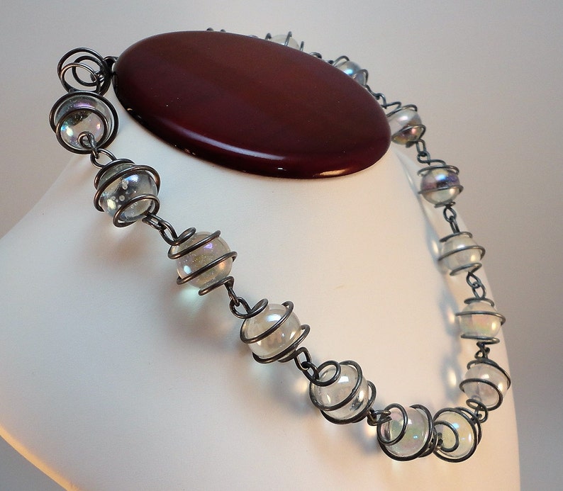 May include: A silver necklace with iridescent glass beads encased in wire. The beads are round and have a subtle shimmer.