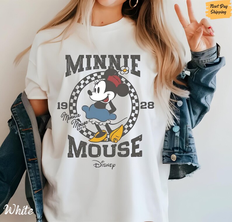 K&ouml;nnte beinhalten: Wei&szlig;es T-Shirt mit einem Vintage-Grafikdruck von Minnie Mouse. Die Grafik zeigt Minnie Mouse in einem roten Kleid und gelben Schuhen, mit dem Text "Minnie Mouse" und "Disney" in einer verwitterten Schriftart.