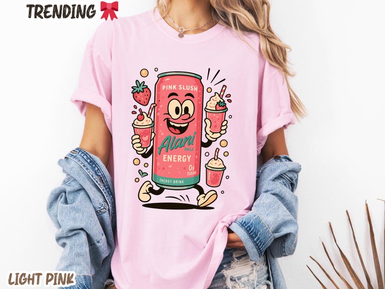 May include: Light pink t-shirt featuring a cartoon can of "Pink Slush" energy drink with a smiling face, holding two slushie cups. The shirt also has the words "TRENDING" and "LIGHT PINK" printed on it.