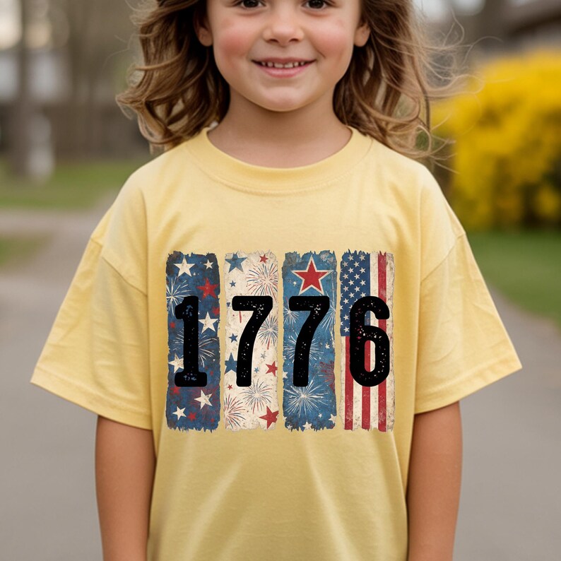 May include: A yellow t-shirt featuring the number "1776" in black. The numbers are set against a backdrop of patriotic designs, including stars, fireworks, and the American flag. The shirt is worn by a person.
