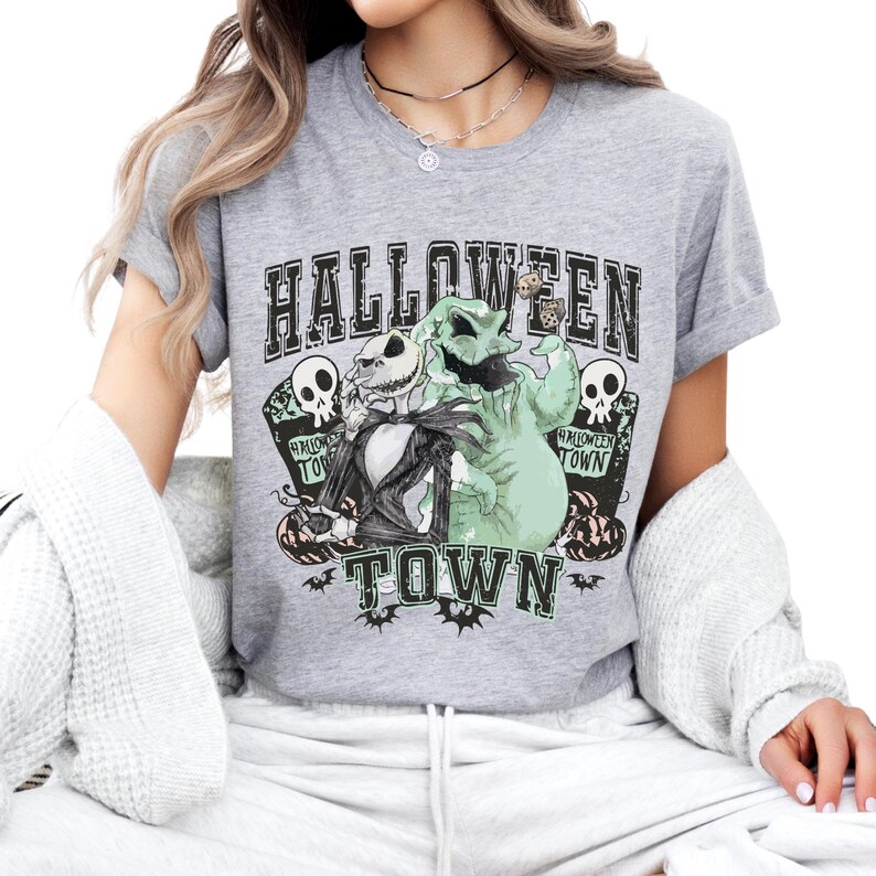 May include: A heather gray short-sleeve t-shirt featuring a graphic print of Jack Skellington and Oogie Boogie from The Nightmare Before Christmas. The design includes the text "HALLOWEEN TOWN," skulls, pumpkins, and bats in black and green.