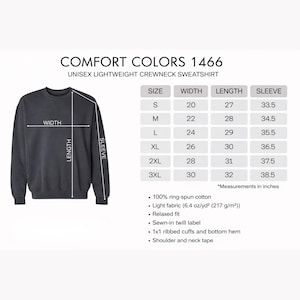 May include: A dark gray unisex crewneck sweatshirt with the text "COMFORT COLORS 1466" and a size chart. The chart provides measurements in inches for width, length, and sleeve length for sizes S through 3XL. The sweatshirt is made of ring-spun cotton.