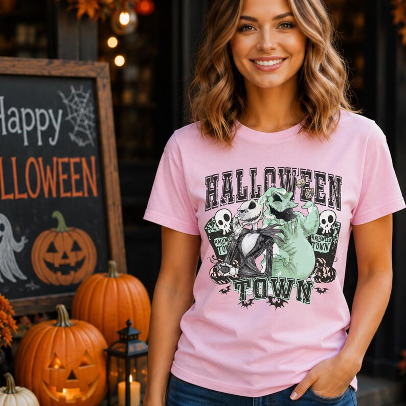May include: A light pink short-sleeve t-shirt featuring a graphic print of Jack Skellington and Oogie Boogie. The text reads HALLOWEEN TOWN. The design includes skulls, tombstones, and small bats, rendered in black, white, and pale green colors.