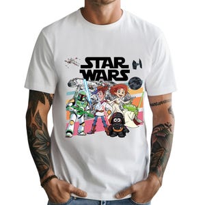 May include: White t-shirt featuring the Star Wars logo in black block letters above a colorful cartoon graphic of Star Wars characters. The graphic includes Boba Fett, Woody, Jessie, and other characters.