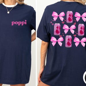 May include: Navy blue t-shirt with the word "poppi" in pink on the front. The back of the shirt features pink bows, pink soda cans, and small pink hearts. The shirt is a casual, comfortable style.