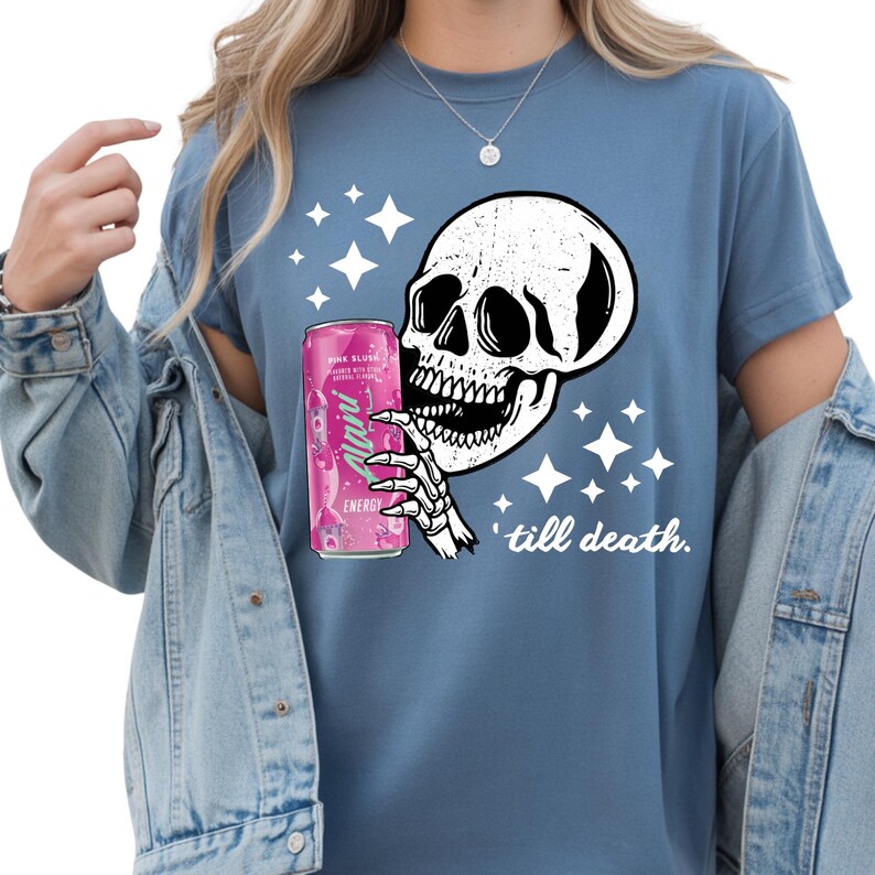 May include: Blue t-shirt featuring a white skull graphic holding a pink energy drink can. The design includes white stars and the text "till death."