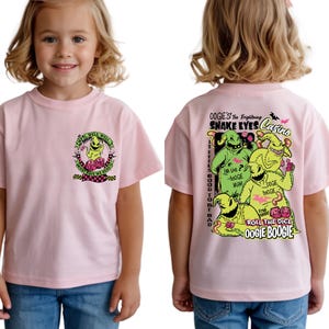 May include: A light pink t-shirt featuring a cartoon graphic of a character with the text "WELL WELL WELL WHAT HAVE WE HERE" on the front. The back of the shirt has a graphic with the text "OOGIE'S Too Frightening SNAKE EYES Casino".