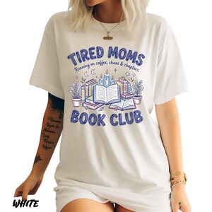 May include: White t-shirt with a blue graphic that reads "TIRED MOMS BOOK CLUB" with illustrations of books, candles, and plants. The text "Running on coffee, chaos & chapters" is also included. The word "WHITE" is printed at the bottom.