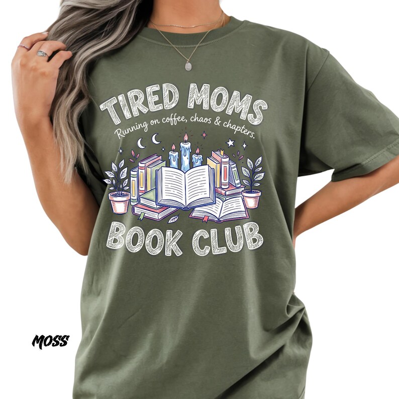 May include: Moss green t-shirt with the text "TIRED MOMS BOOK CLUB" in a white, distressed font. The graphic features books, candles, and plants. The phrase "Running on coffee, chaos & chapters" is also included.