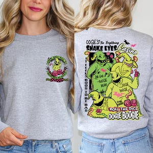 May include: A heather gray sweatshirt featuring a colorful graphic of Oogie Boogie from The Nightmare Before Christmas. The front has a small design, while the back displays a larger, detailed image with text including "Snake Eyes Casino."