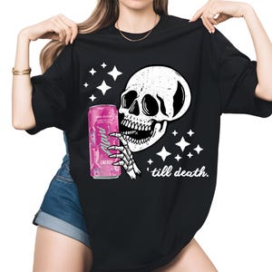 May include: Black t-shirt featuring a white skull graphic holding a pink energy drink can. The design includes white stars and the phrase "'till death." The can has the text "Alani Energy".