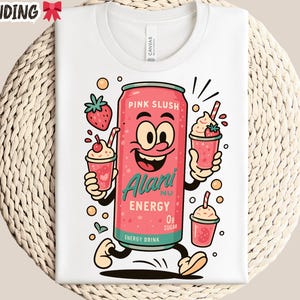 May include: White t-shirt featuring a cartoon pink energy drink can with a smiling face, holding two strawberry slushies. The can reads "Pink Slush" and "Alani Nu Energy 0g Sugar". The shirt has the word "TRENDING" at the top.