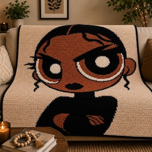 May include: A crocheted blanket featuring a cartoon character with a determined expression. The blanket has a tan background with a large graphic of a character in black and brown. The border is black.