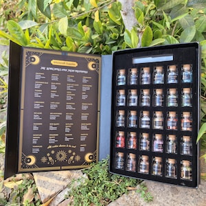 May include: A black box set of witchcraft supplies, open to reveal small glass bottles with cork stoppers, each containing a different crystal. The left side of the box has a list of crystals and their properties. The text reads "Witchcraft Supplies".