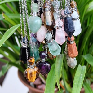 Op de afbeelding: Een verzameling kristallen fles kettingen met verschillende edelsteen stoppen, waaronder amethist, tijgeroog, rozenkwarts en groene aventurijn.
