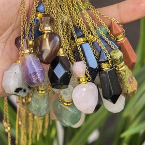 Op de afbeelding: Een verzameling edelsteen hangerkettingen met goudkleurige kettingen. De hangers hebben verschillende vormen en kleuren, waaronder hart-, zeshoekige en rechthoekige ontwerpen. De edelstenen omvatten amethist, rozenkwarts en zwarte obsidiaan.