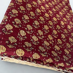 Puede incluir: Textil granate doblado con un patr&oacute;n repetido de dise&ntilde;os florales amarillos. La tela est&aacute; cosida con hilo blanco y los bordes son de color beige claro.